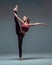 Flexible young female dancer practices stretching in stylish sportswear barefoot in studio  on gray background