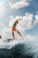 Flexible young woman in colorful swimsuit energetically balancing on wave on wakesurf board.