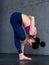 Flexible young woman performing one-leg balance exercise doing half bound lotus standing forward fold pose indoors