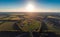 Flight above summer landscape: forest, green fields at countryside in hot air balloon or drone at sunset, aerial view