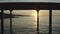 A flight of the camera along a wooden pier with dark pillars flying by in the background light and the water flashing