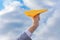 flight, freedom concept, a hand holds a bright yellow paper plane against a blue sky