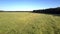 Flight over green grass meadow to operating tractor