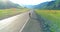 Flight over hitchhiker tourist walking on asphalt road. Huge rural valley at summer day. Backpack hiking guy.