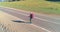 Flight over hitchhiker tourist walking on asphalt road. Huge rural valley at summer day. Backpack hiking guy.