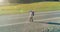 Flight over hitchhiker tourist walking on asphalt road. Huge rural valley at summer day. Backpack hiking guy.