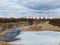 Flight over the river in the spring park. Remnants of ice are visible. In the distance, people are walking along the alleys