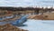 Flight over the river in the spring park. Remnants of ice are visible. In the distance, people are walking along the alleys