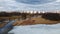 Flight over the river in the spring park. Remnants of ice are visible. In the distance, people are walking along the alleys