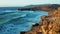 Flight over wide ocean waves crashing among huge rock formations. Sunset light. Turquoise water foaming. Aerial