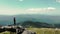 Flight over a woman standing on top of a mountain and looking into the future. Mountain top with big stones and a young