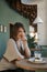 Flirtatious girl sits at table in cafe. Young woman in cafe with cup of latte or cappuccino and dessert