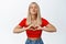 Flirty blond girl shows kissing face and heart sign, standing over white background in stylish summer clothes