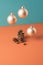 Floating Christmas tree gold baubles with tree cones underneath against two tone pastel background.