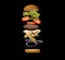 Floating layered grilled cheeseburger ingredients with a beef patty, cheese, salad on toasted bun over black background