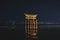 The floating Torii Gate of Itsukushima Shrine Illuminated in the night in front of city lights in Miyajima, Hiroshima, Japan