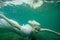 A floating woman. Underwater portrait. Girl in white dress swimming in the lake. Green marine plants, water