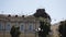 A flock of pigeons flies among the city and sits on the facade of the building