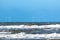 A flock of seabirds close above a stormy with spindrift waves and an offshore windmill park