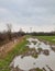 Flooded and deeply rutted field track alongside a swollen river.
