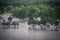 Flooded houses and trees in low area in front of leafy hill with brown swirling waters