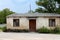 Floor level small abandoned structure building with dilapidated cracked wooden window blinds and doors surrounded with gravel and