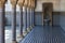 The floor and walls are lined with blue tiles, columns and arches on the left, a drinking water fountain in the corner.