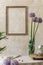 Floral composition at kitchen interior with wooden family table, beautiful flowers in vase, plates, cups, tray.