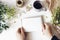 Floral lifestyle composition. Mockup scene with mums flowers, greenery and cup of coffee on white table. Female hands