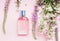 Floral perfume bottle with fresh herbs and flowers on pink background, top view.