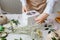 A florist decorates a gift box with flowers and a ribbon on a white desktop. Only the hands are in the frame