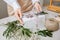 A florist decorates a gift box with flowers and a ribbon on a white desktop. Only the hands are in the frame