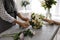 Florist tieing bow of beautiful wedding bouquet at light grey marble table, closeup