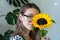 Florist woman in glasses holding and hiding behind a sunflower, looking at camera, close up