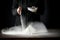 Flour on a kitchen table on a black moody background in the morning light. Woman`s hands sieving flour through a sieve.