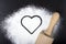 Flour and rolling pin with a heart symbol. Flour on a black back