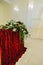 Flower arrangement with greenery, red and white roses on a stand with a bright red velvet fabric.