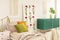 Flower board between single bed with olive green, orange and pastel pink pillows and green wooden cabinet with leaf in glass vase