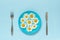 Flower chamomile daisy on blue plate and cutlery fork knife on blue paper background Concept vegetarianism, healthy eating or diet