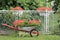 Flower garden with carts. White stroller with red handles, in it red flowers. Flower carts