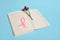 Flower and pink ribbon, symbol of Breast Cancer Awareness Day, lying on a page with a line of notepad with inscriptions reminding