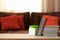 Flower pot and book stack on wooden table against defocused sofa with pillows. Front view