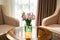 Flower vase on round table with two soft chairs, next to window with golden color curtain in the interior of the hotel