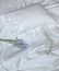 Flowers on the messy bed, white bedding items and blue flowers bouqet