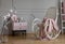 Flowers and rocking chair with blanket in grey and pink living room interior with cabinet. Real photo