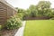 Flowers, trees and green grass in the garden of house with wooden screen. Real photo