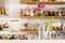 Flowers in vases in a white kitchen with wooden shelves stocked with spices