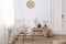 Flowers on wooden stool next to armchair in white loft interior with pouf and plate. Real photo