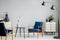 Flowers on wooden table between blue armchairs in grey flat interior with black lamp.