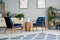 Flowers on wooden table between blue armchairs in grey flat interior with carpet and posters. Real photo